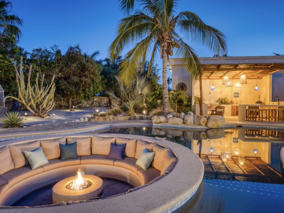 Casa Tres Palmas courtyard at twilight with fire pit, illuminated pool, and outdoor kitchen