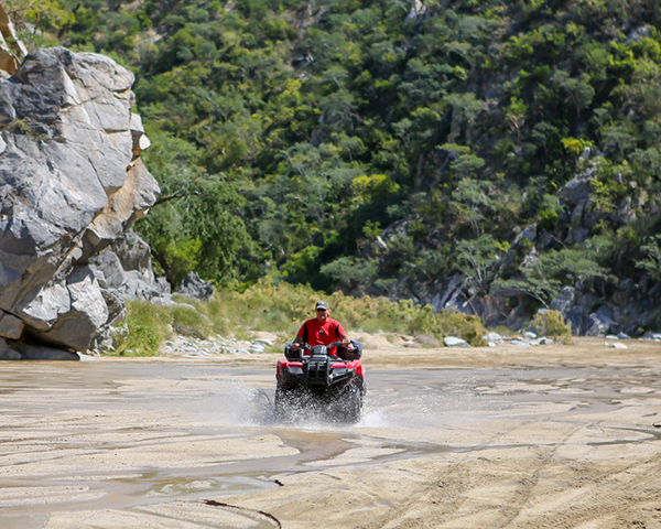 ATV rider splashing through a desert river crossing